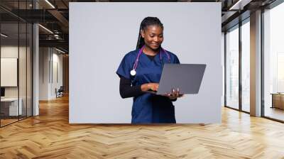 Beautiful African American woman doctor or nurse holding a laptop computer on a white background Wall mural